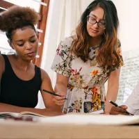 Diverse group of women collaborating round a table, using pens and paper