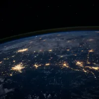 The darkened surface of the Earth at night, as seen from space, with lit-up cities visible.