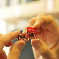 Hand holding a red internet of things circuit board created by the Centre for IoT and Pervasive Systems. 