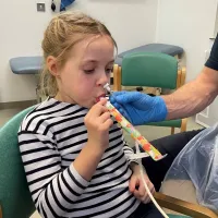 Young girl with a tube up her left nostril, blowing a party blower